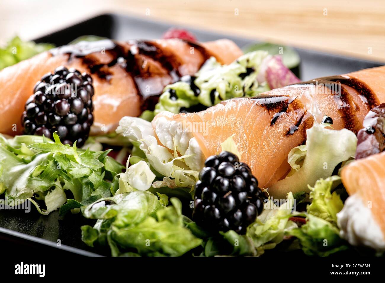 Nahaufnahme von schmackhaften Lachsbrötchen gefüllt mit Frischkäse und Garniert mit Sauce auf dem Teller mit frischem Salat serviert und Brombeeren Stockfoto