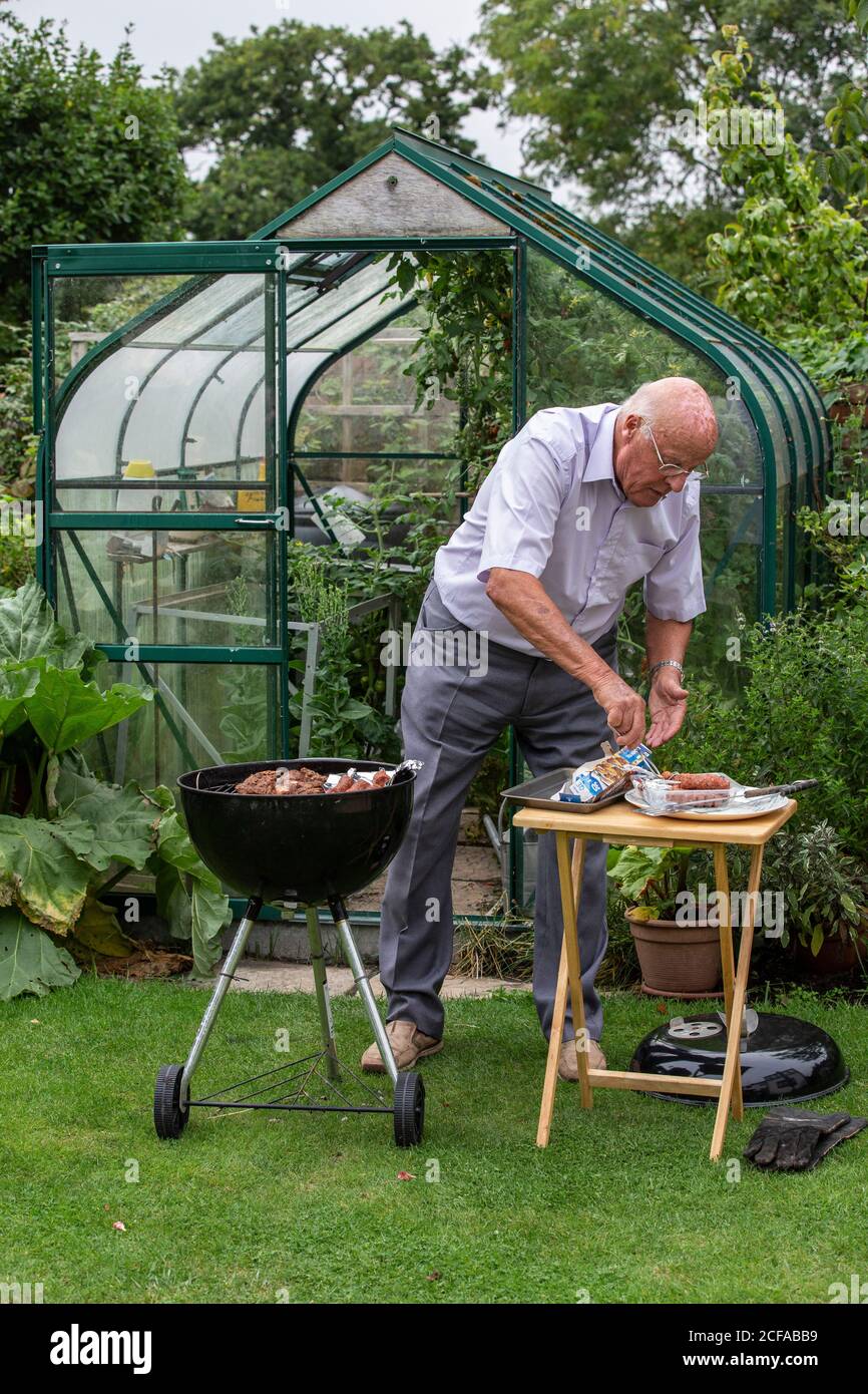 Rentner im Ruhestand in seinen 80ern genießen das Leben im Freien Grillen und essen gesundes Gemüse aus eigenem Anbau während der Coronavirus Sperre, Somerset UK Stockfoto
