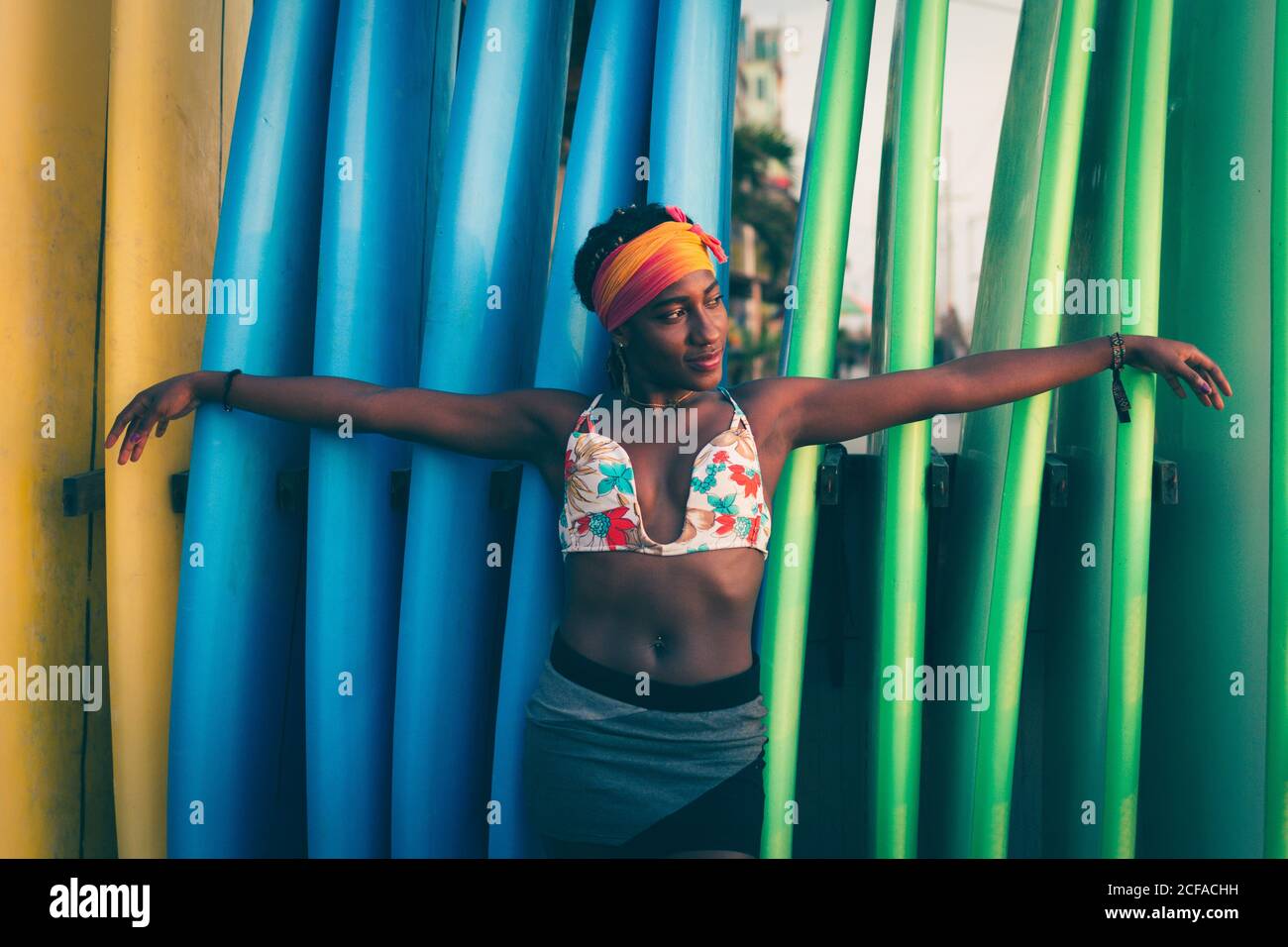 Junge afroamerikanische Frau trägt bunte Bikini-Top und Stirnband Spreizen  Sie die Arme, während Sie sich auf farbenfrohe Surfbretter zurücklehnen  Stockfotografie - Alamy