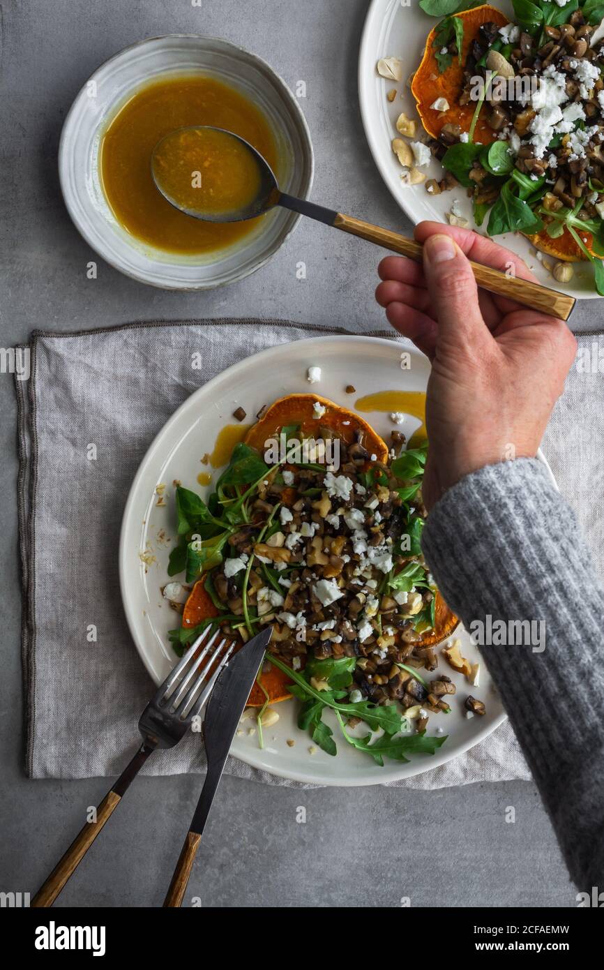 Von oben unkenntlich Person, die Löffel Sauce für lecker Salat während der Zubereitung des Mittagessens auf einem grauen Tisch Stockfoto