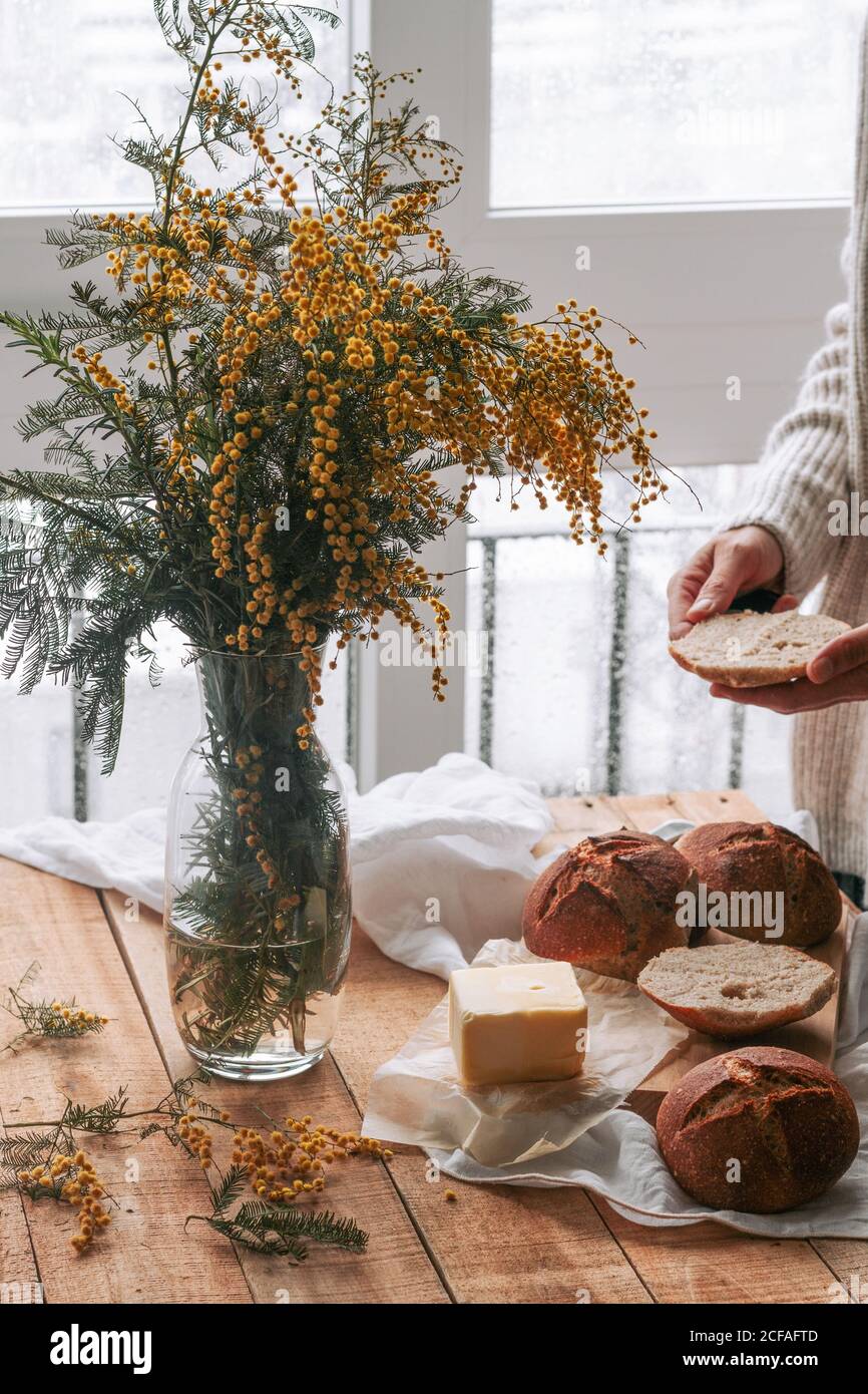 Gesichtslose Dame, die Butter auf Brot in der Küche verteilt Stockfoto