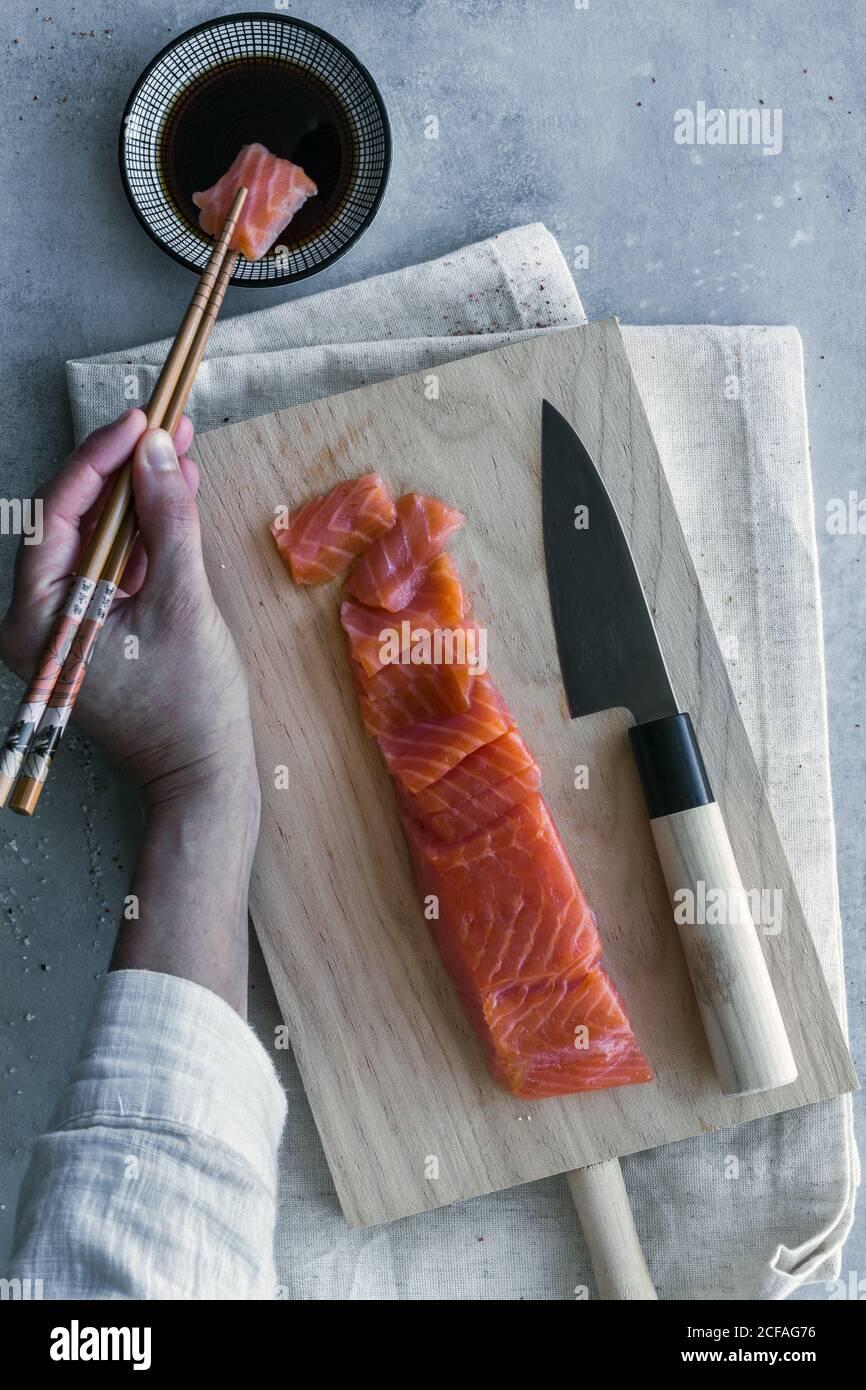 Von oben Ernte anonyme Person hält Stück Lachs mit Essstäbchen und Dipping in Sauce am Tisch serviert Stockfoto