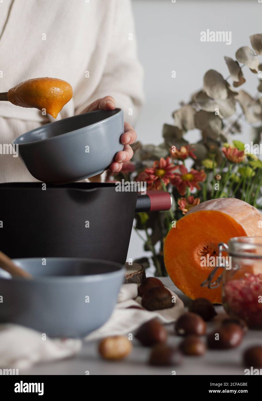 Crop kochen mit Suppenschüssel und Löffel in den Händen Kochen Kürbis- und Kastaniensahnesuppe Stockfoto