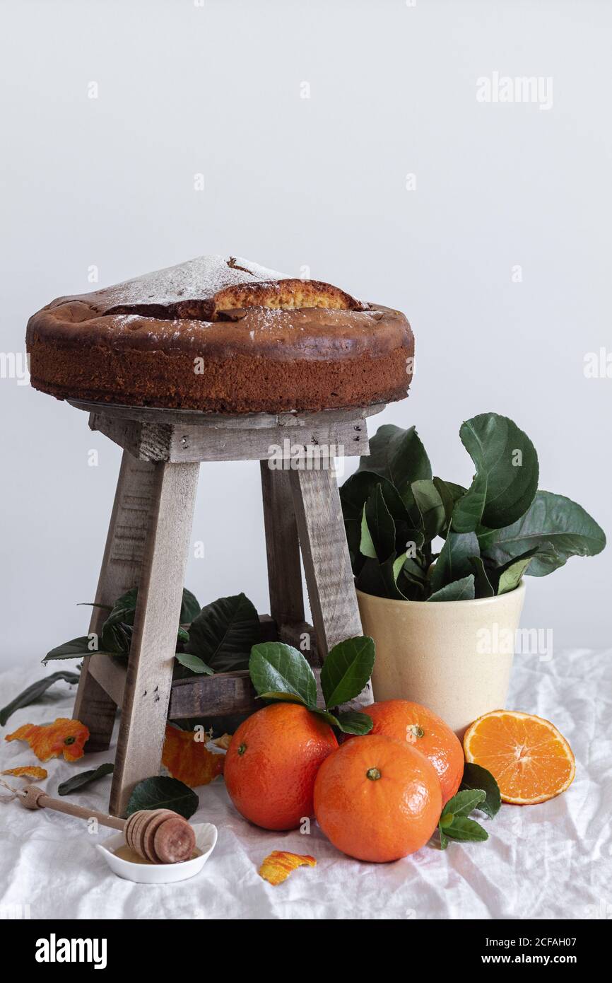 Malerisches Stillleben von frischem appetitlichen Schnitt und ganze Mandarine Frischer leckerer Kuchen auf kleinem Holzhocker und grüner Pflanze Im Topf Stockfoto