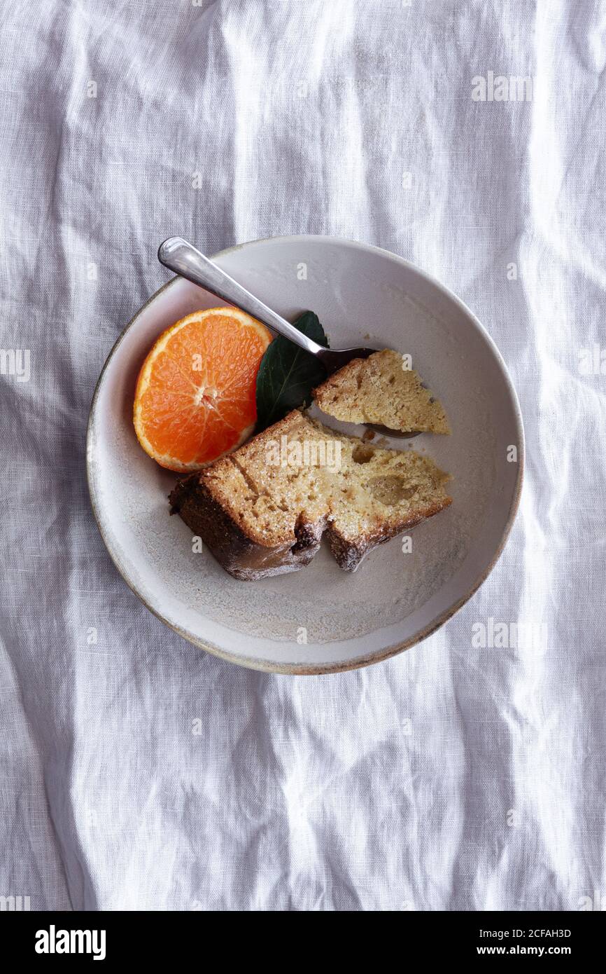 Von oben appetitlich süßer Kuchen und reife orange Mandarine geschnitten Und serviert auf weißem Teller auf dem Tisch Stockfoto