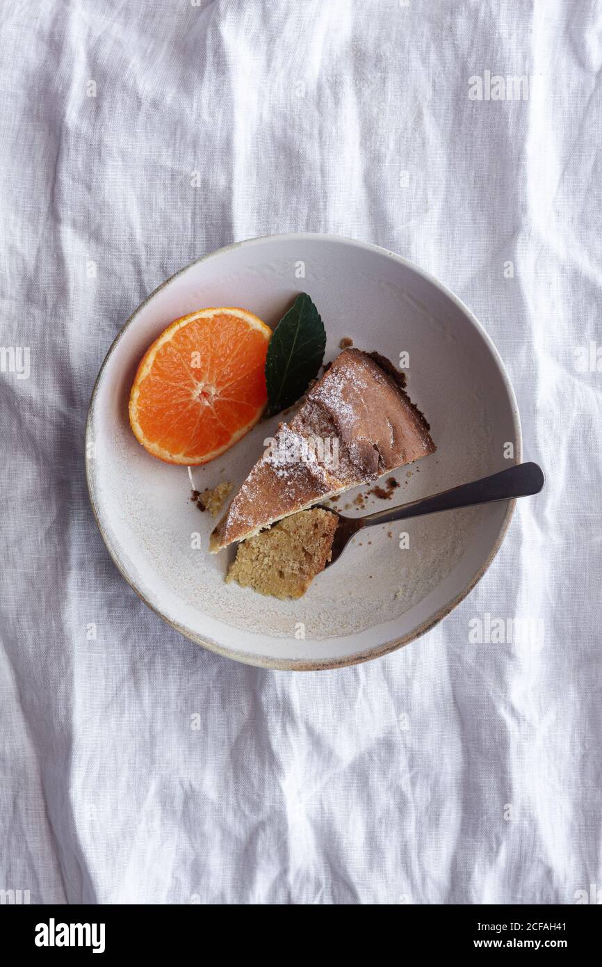 Von oben appetitlich süßer Kuchen und reife orange Mandarine geschnitten Und serviert auf weißem Teller auf dem Tisch Stockfoto