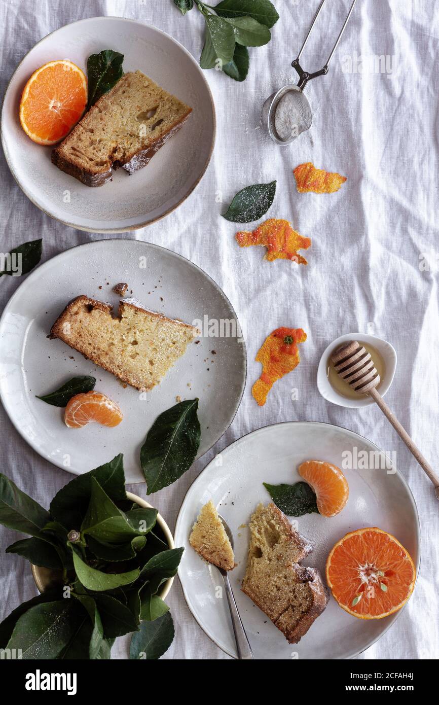 Von oben appetitlich süßer Kuchen und reife orange Mandarine geschnitten Und serviert auf weißen Tellern auf einem mit Pflanzen dekorierten Tisch Stockfoto