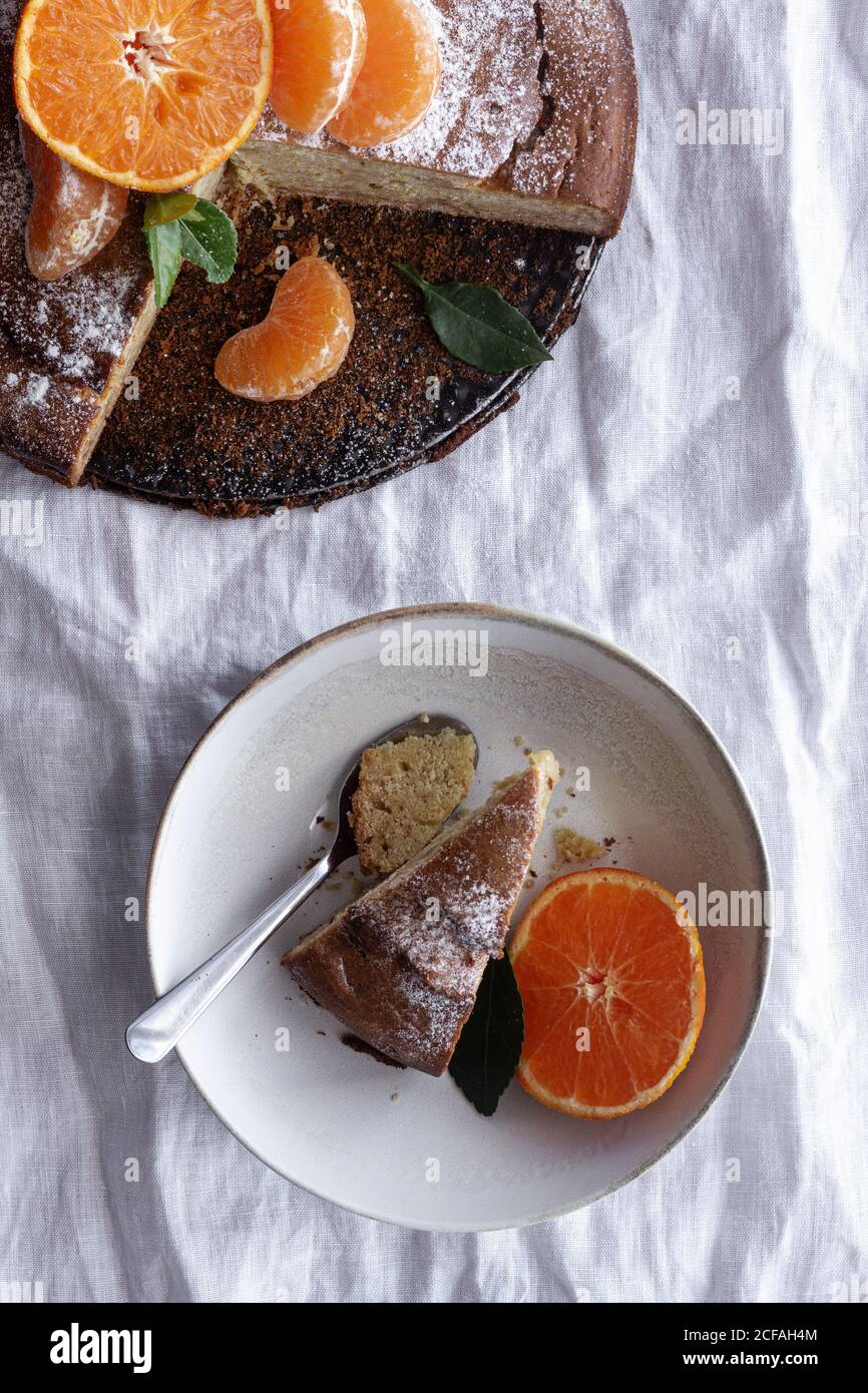 Von oben appetitlich süßer Kuchen und reife orange Mandarine geschnitten Und serviert auf weißem Teller auf dem Tisch Stockfoto