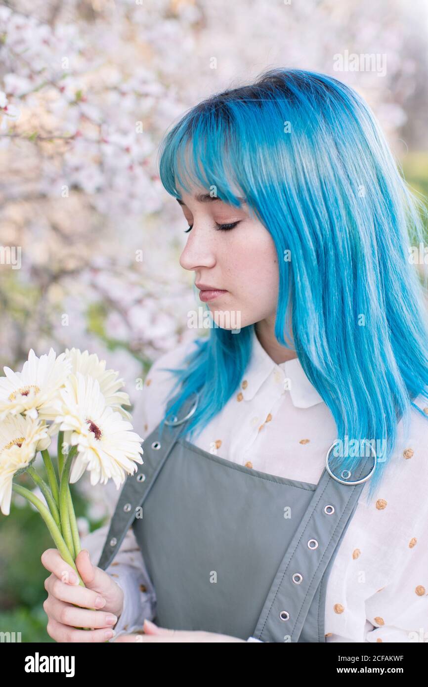 Moderne trendige Frau mit blauen Haaren halten und betrachten Blumenstrauß im blühenden Frühlingsgarten Stockfoto