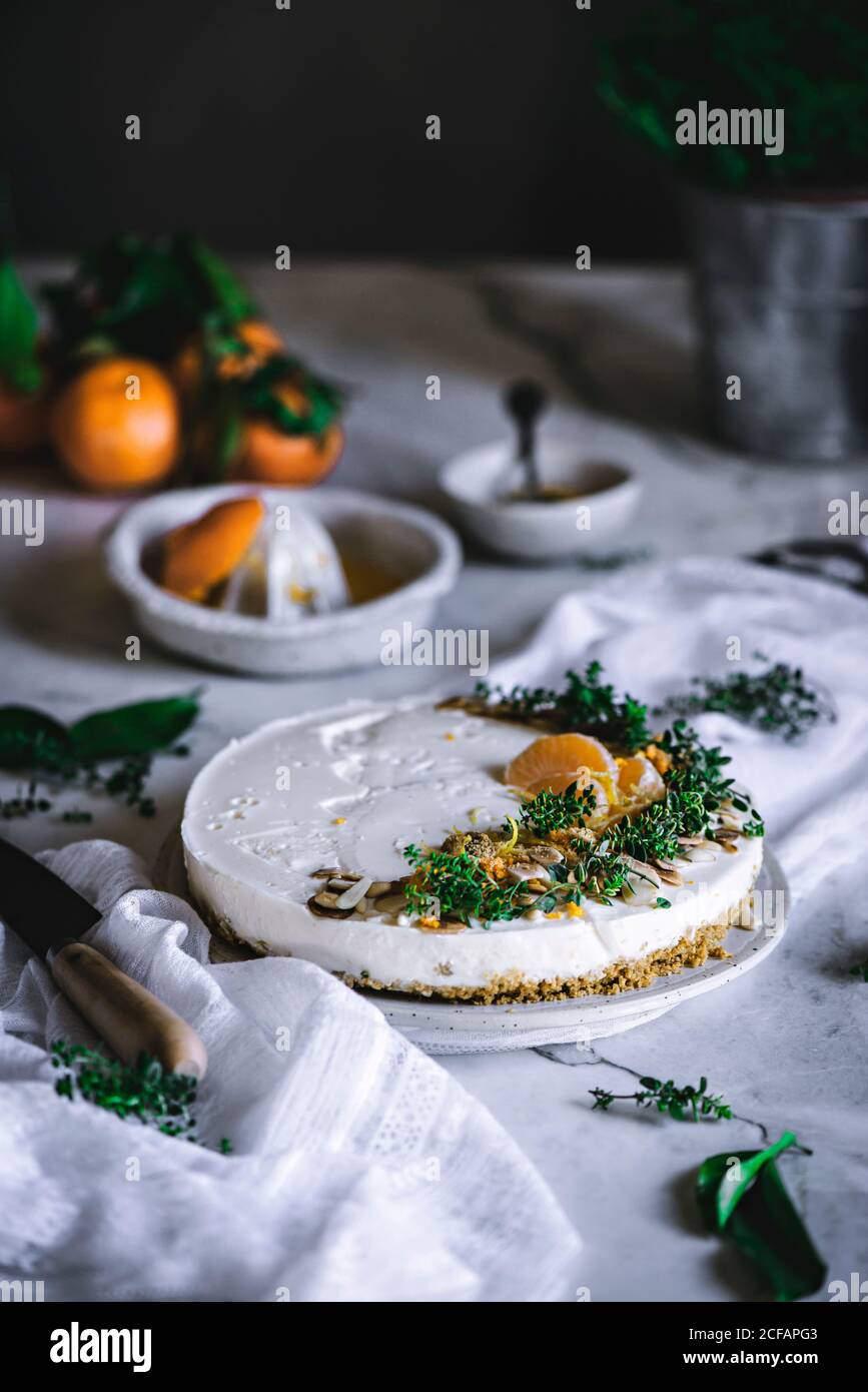 Von oben schmackhaft appetitlich dekoriert mit Mandarinengrün und Nüssen Mandarine Kuchen und ganze Zitrusfrüchte Messer Schüssel mit Löffel auf Tabelle Stockfoto