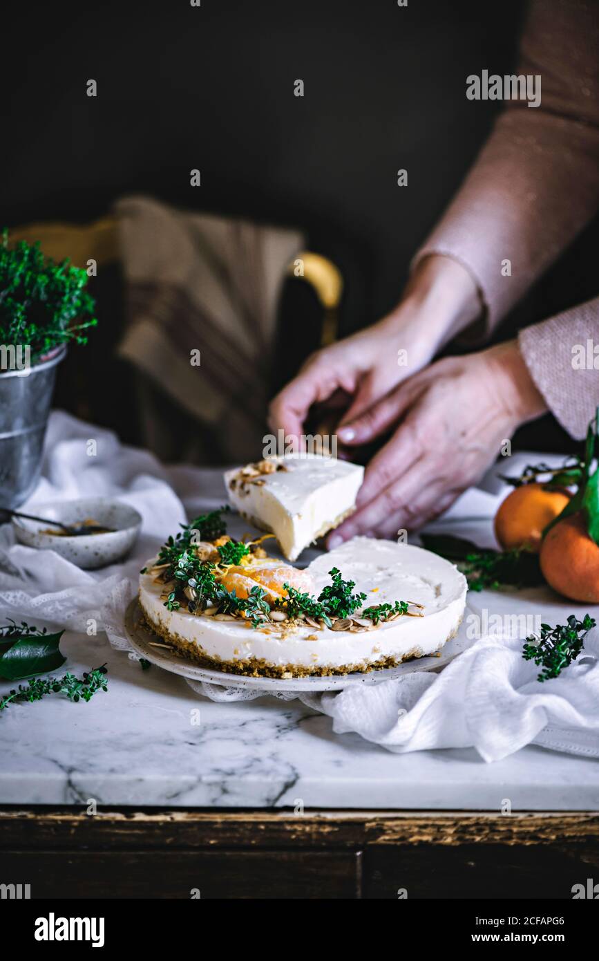 Weiße cremige leckere Mandarine Kuchen mit grünen und Zitrusfrüchten dekoriert Auf dem Tisch schneiden von den Händen kochen Stockfoto