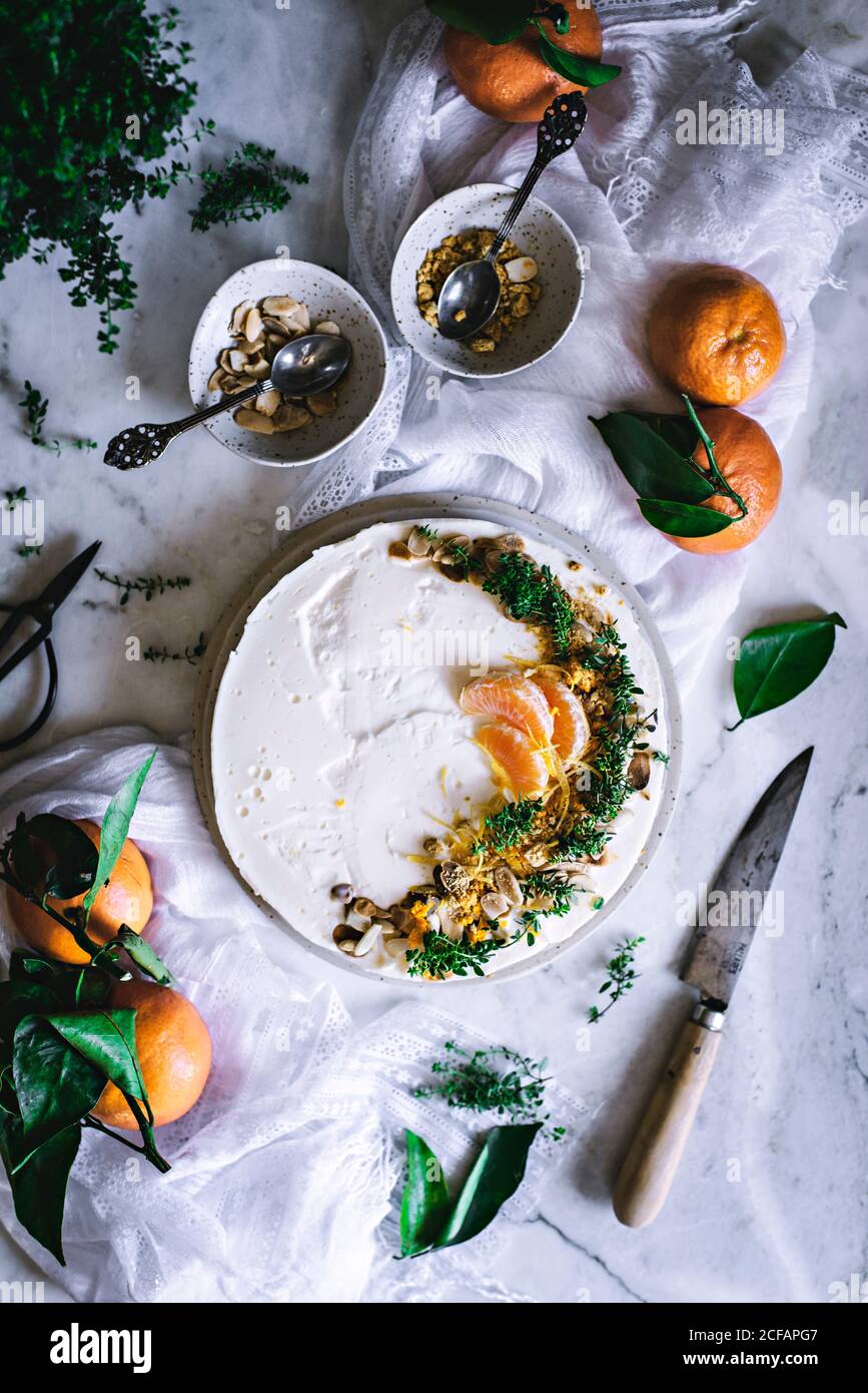 Von oben schmackhaft appetitlich dekoriert mit Mandarinengrün und Nüssen Mandarine Kuchen und ganze Zitrusfrüchte Messer Schüssel mit Löffel auf Tabelle Stockfoto
