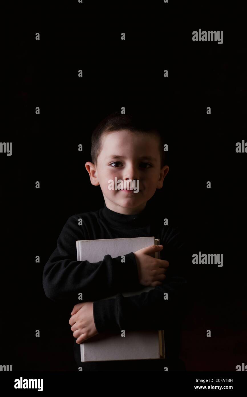 Liebenswert ernst Kind in Freizeitkleidung halten Tablet in den Händen Und die Kamera mit entschlossenem Blick isoliert auf schwarz Hintergrund Stockfoto