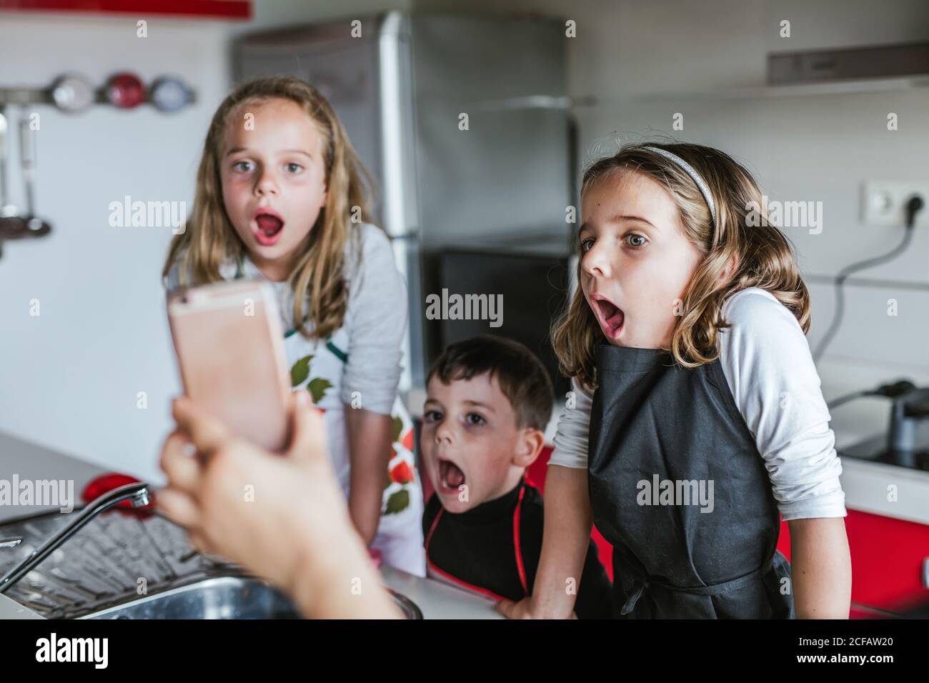 Drei Kinder erstaunt Blick auf den Bildschirm des Smartphones in Ernte Hand, während sie zusammen in der Küche stehen Stockfoto