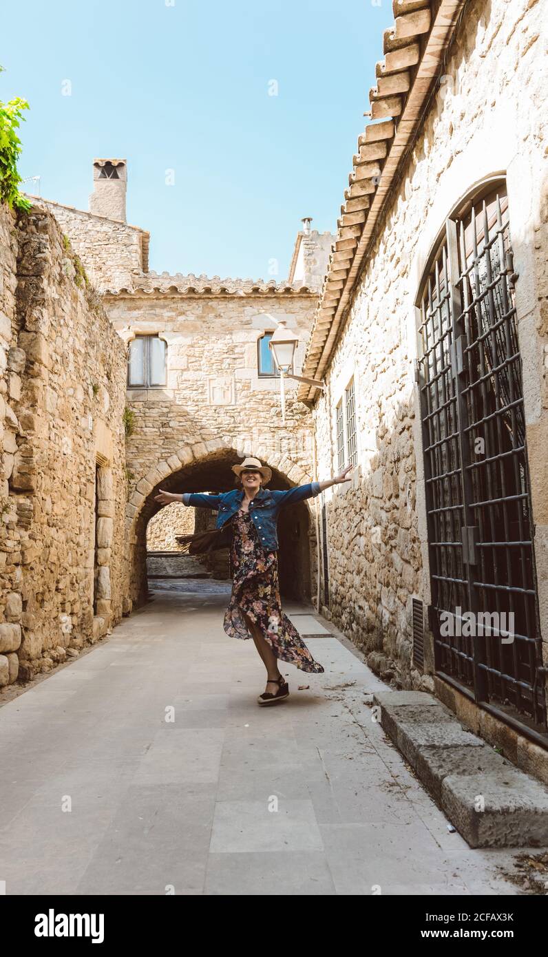 Frau in Kleid und Hut ausstreckt Arme, Besuch der Straßen eines mittelalterlichen Dorfes mit Wandkletterer Pflanze in Europa Stockfoto