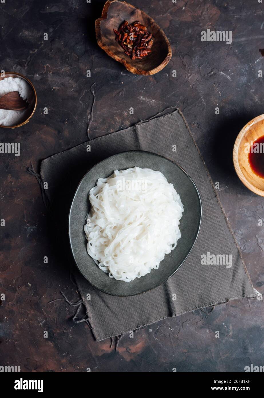Draufsicht auf Schüssel mit gekochten Reisnudeln Tisch neben Schüsseln mit Sauce und Gewürzen bei der Zubereitung von Speisen In der Küche Stockfoto