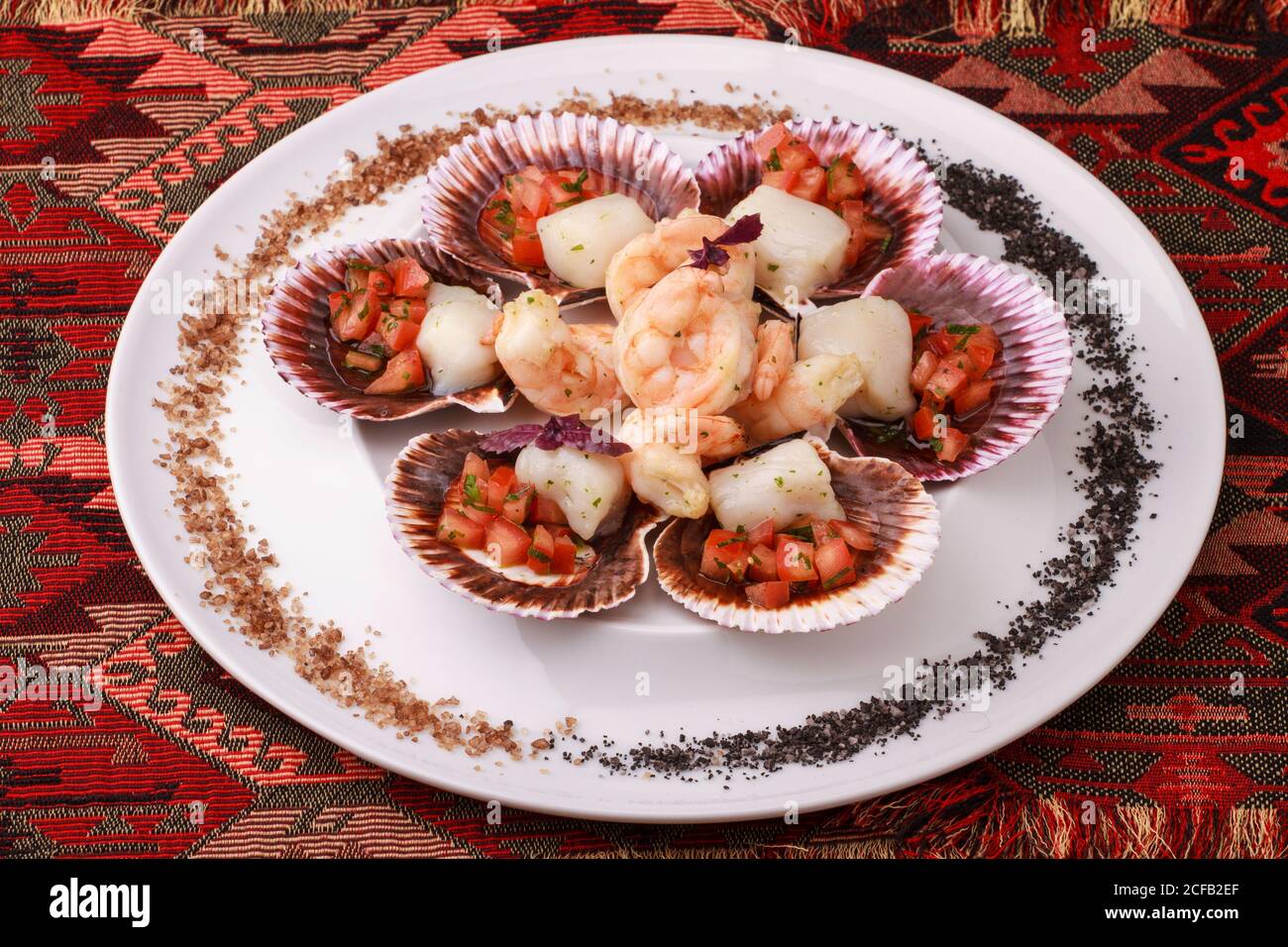 Gemischter Teller mit Meeresfrüchten (Jakobsmuscheln mit Tomatensalsa und Garnelen), serviert mit violettem und schwarzem Salz. Stockfoto