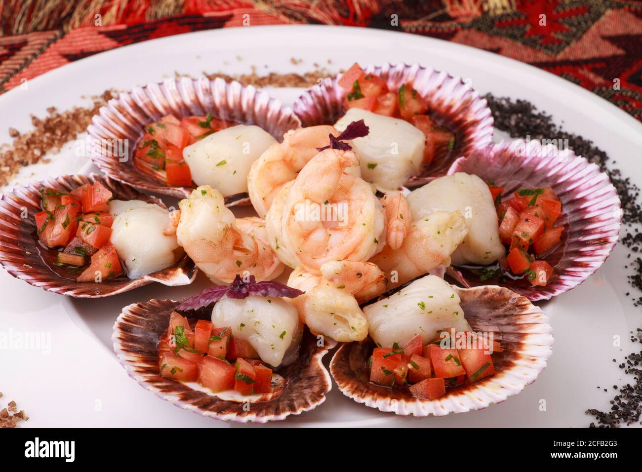 Gemischter Teller mit Meeresfrüchten (Jakobsmuscheln mit Tomatensalsa und Garnelen), serviert mit violettem und schwarzem Salz. Stockfoto