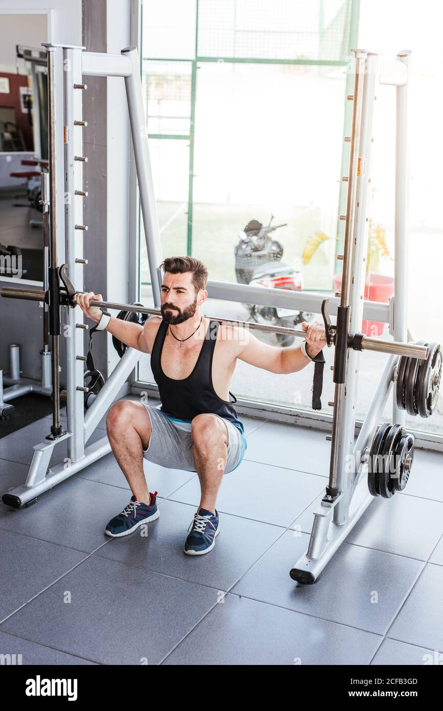Kraftvoller entschlossener Sportler, der mit Langhantel an der Hocke trainiert Beim Gewichtheben mit Personal Coach im modernen Fitnessstudio Stockfoto