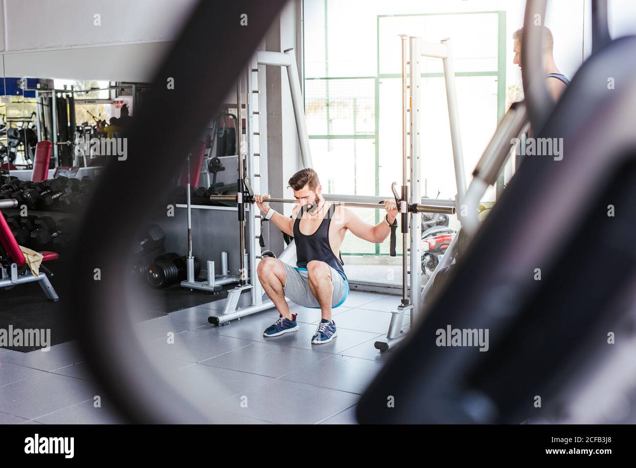 Kraftvoller entschlossener Sportler, der mit Langhantel an der Hocke trainiert Beim Gewichtheben mit Personal Coach im modernen Fitnessstudio Stockfoto