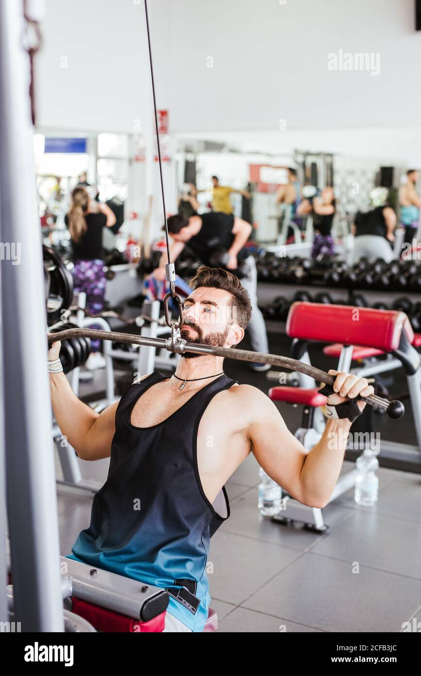 Kraftvoller entschlossener Sportler, der mit Langhantel an der Hocke trainiert Beim Gewichtheben mit Personal Coach im modernen Fitnessstudio Stockfoto