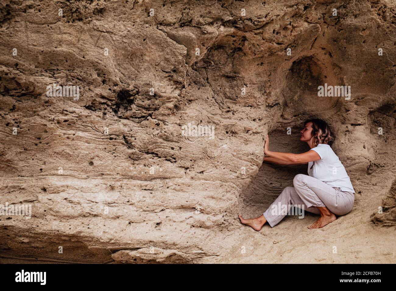 Seitenansicht der barfuß-Frau, die in einer Höhle in Rough sitzt Stein Klippe und meditieren während Tai Chi auf dem Land üben Stockfoto