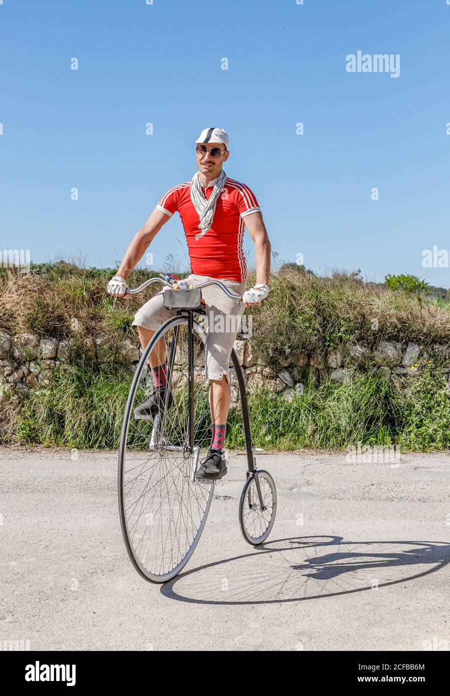 Erwachsene Männer in Sonnenbrillen und stilvolle Freizeitkleidung Reiten Retro High-Rad-Bike entlang Fußweg gegen grüne Wiese in Sommertag Stockfoto