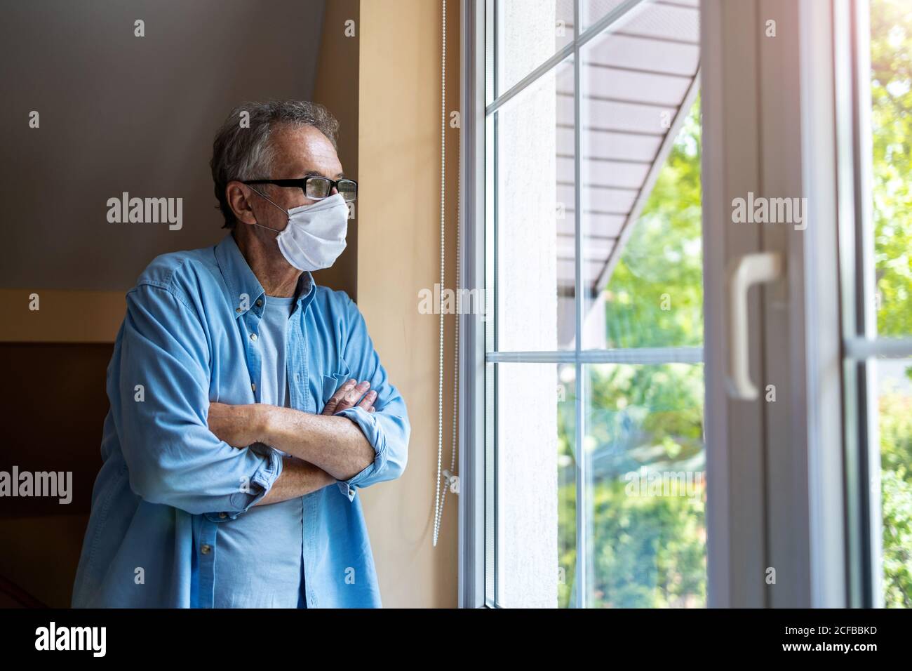 Älterer Mann mit schützender Gesichtsmaske, der aus dem Fenster schaut Stockfoto