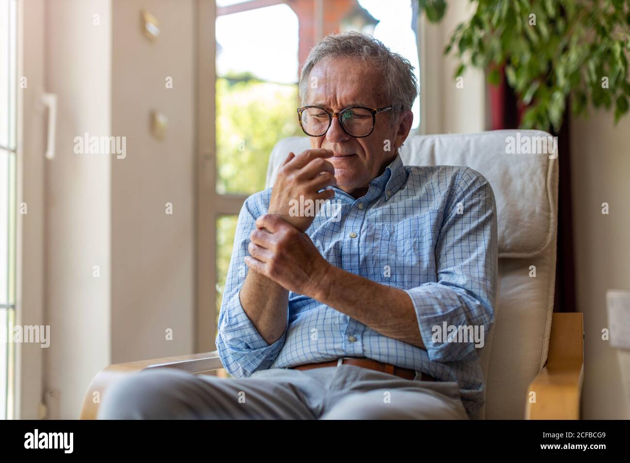 Älterer Mann mit Arthritis, der sich die Hände reibt Stockfoto