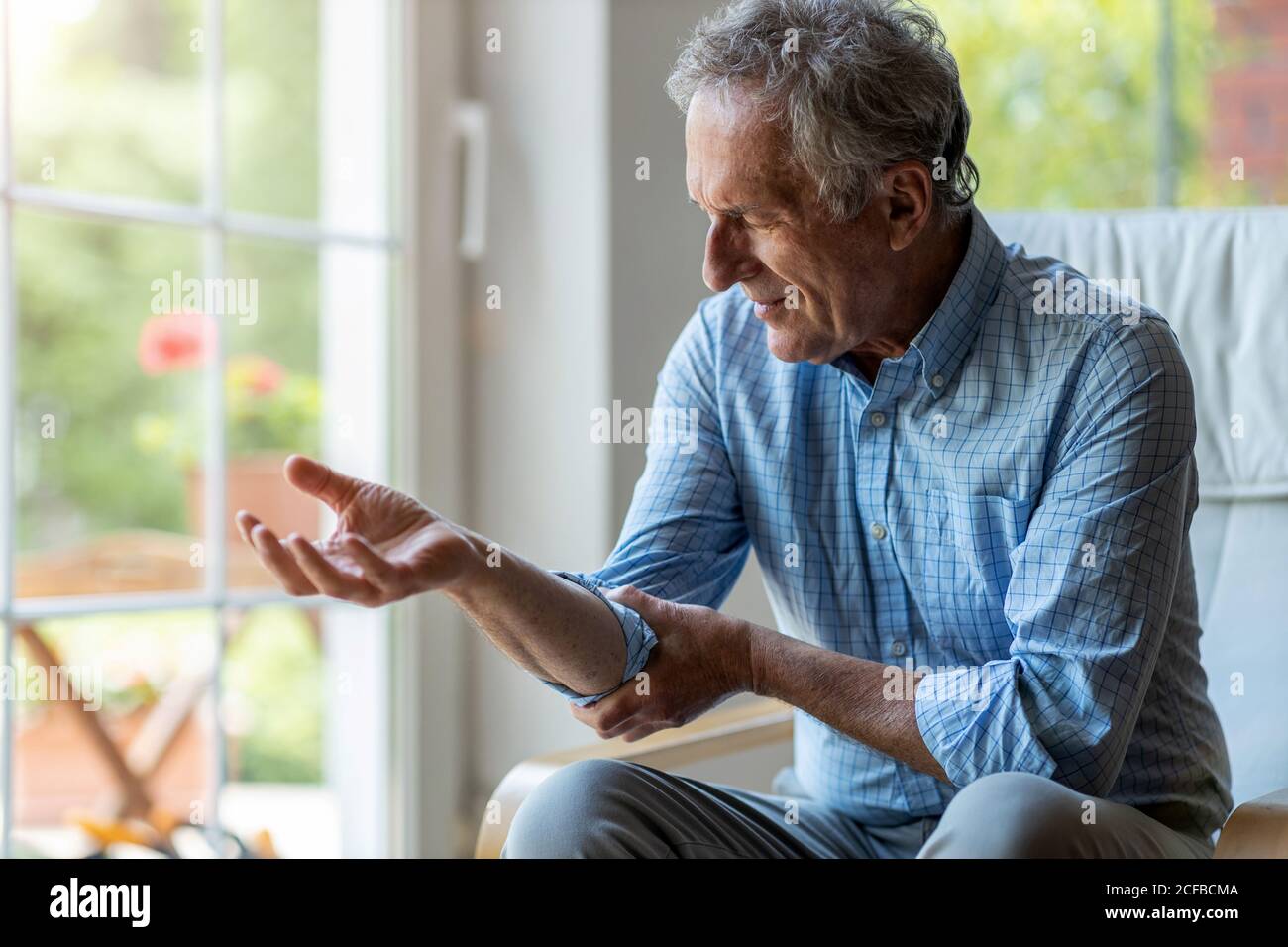 Älterer Mann mit Arthritis, der sich die Hände reibt Stockfoto