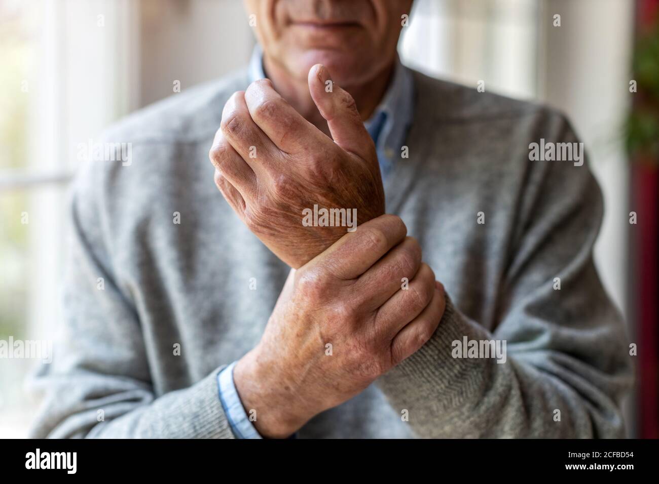 Älterer Mann mit Arthritis, der sich die Hände reibt Stockfoto