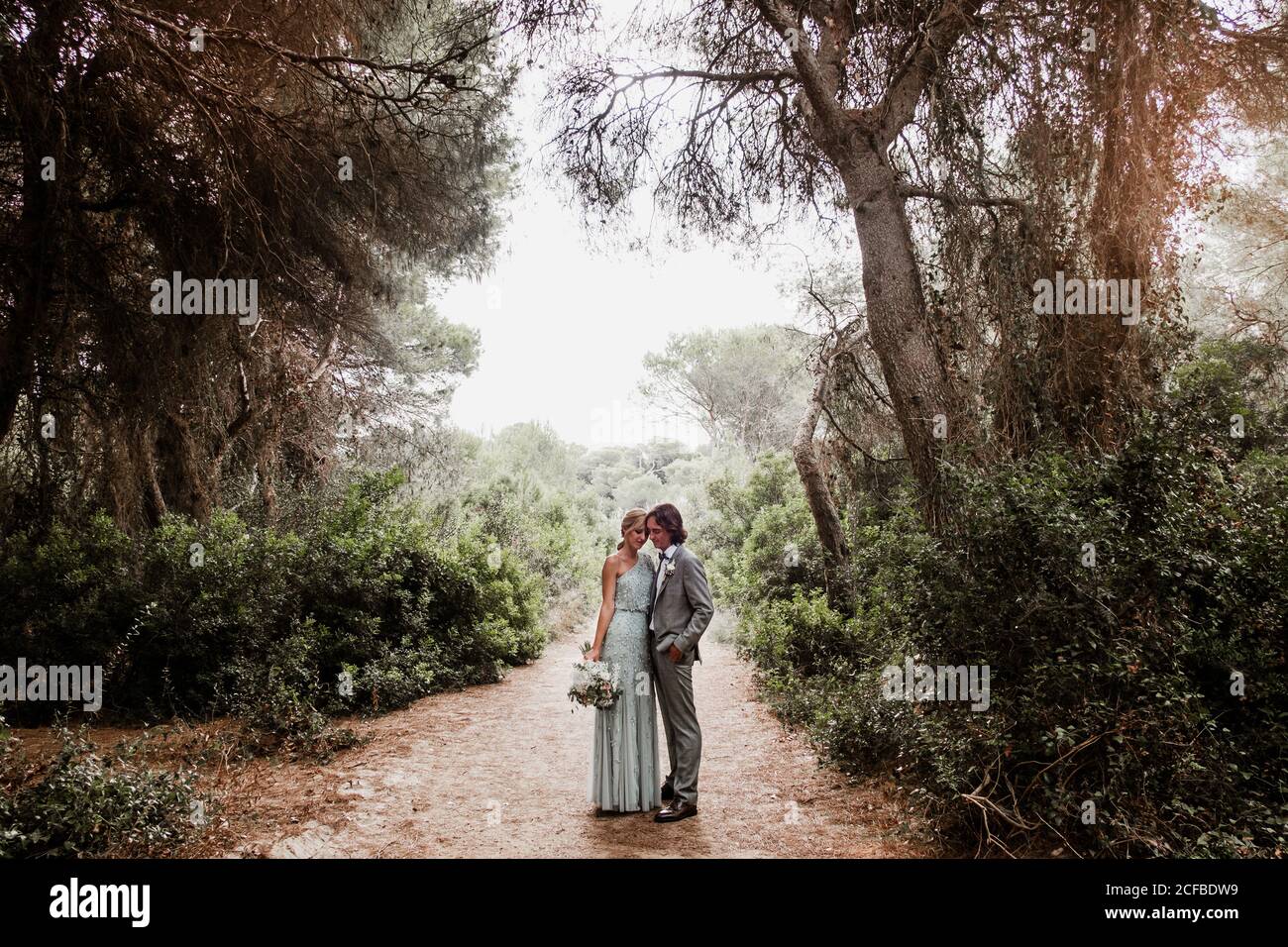 Junge frisch verheiratetes Paar in Hochzeitskleidung stehend und umarmt Auf dem Weg zwischen schönen grünen Wald mit großen Bäumen Stockfoto