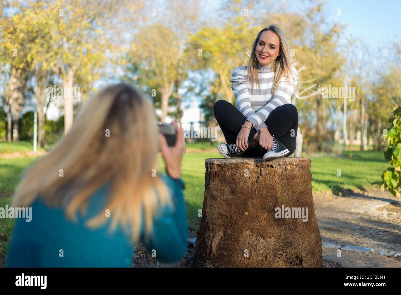 Blonde Mädchen Foto mit Kamera zu ihrem Freund. Auf einem Holzschnitt im Park sitzend. Lächelnd. Stockfoto