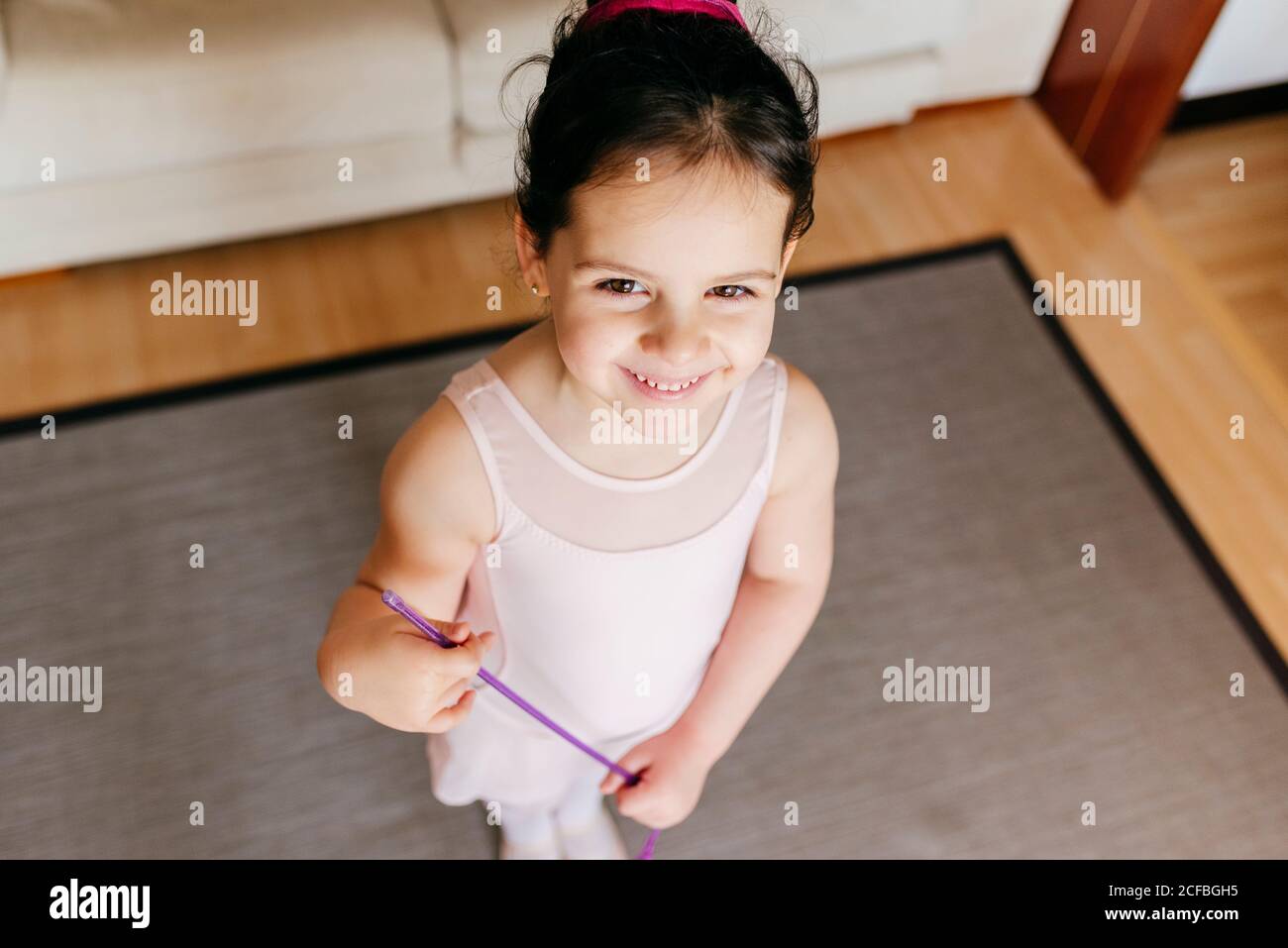 Von oben kleines Mädchen mit Band lächelt für Kamera während Rhythmisches Turntraining zu Hause Stockfoto