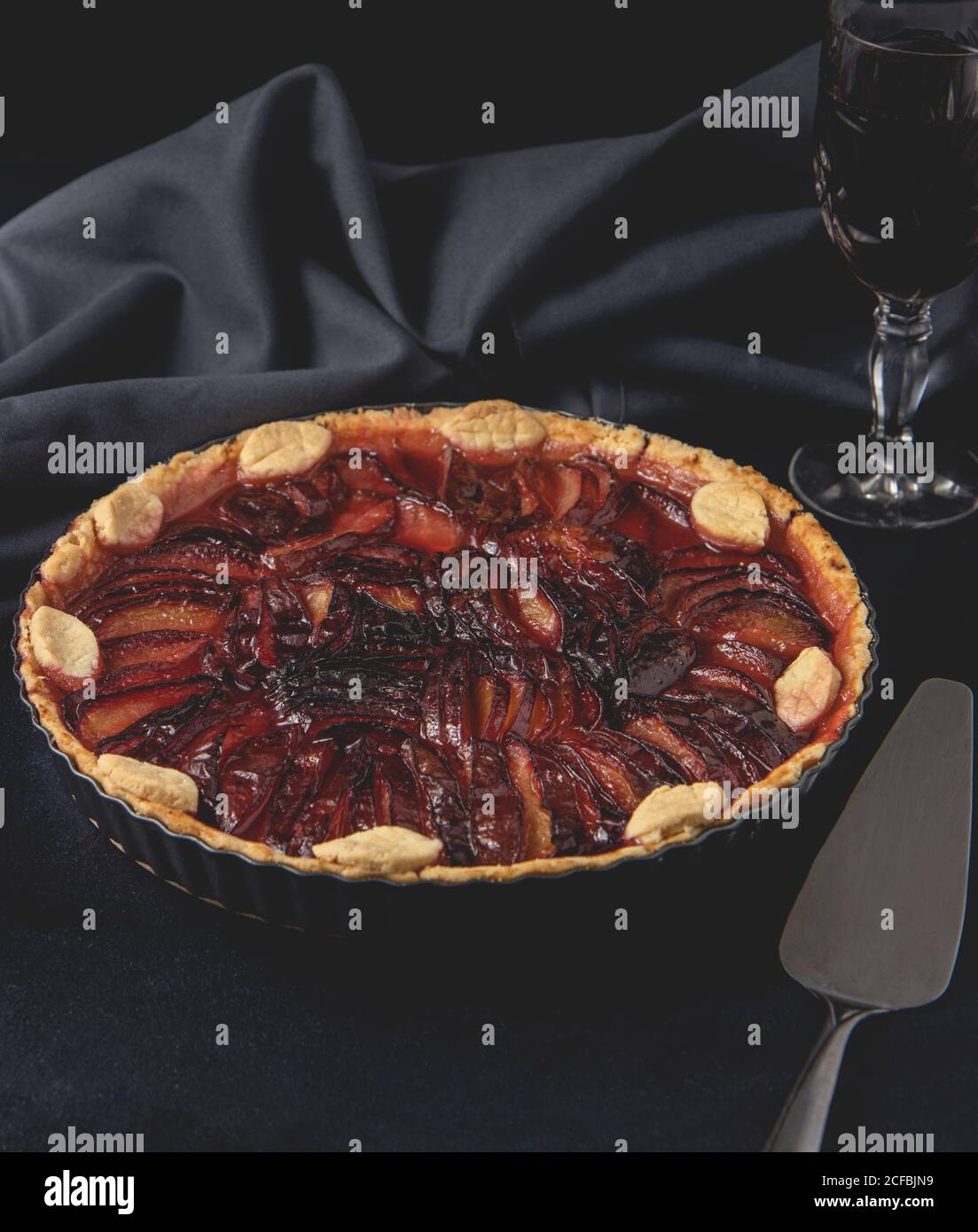 Hausgemachte Kuchen mit Pflaumen auf dem dunklen Hintergrund platziert. Gebackene Tarte mit Pflaumen. Vorderansicht. Stockfoto