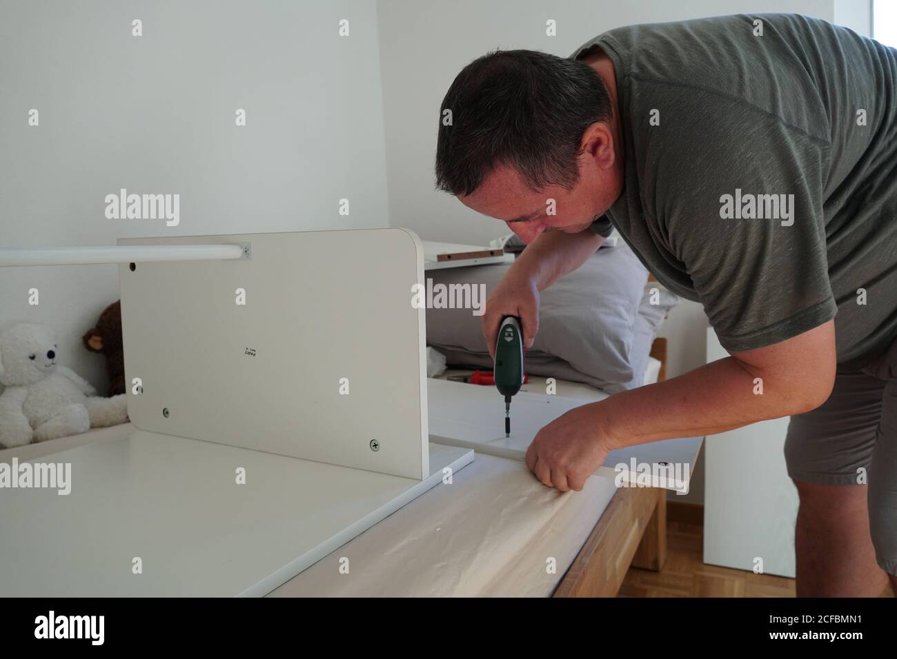 Mann, der Möbel mit einem Akkuschrauber zusammenführt. Er verbessert sein Zuhause mit einem neuen Computertisch. Das DIY-Set wurde in einem Online-Shop bestellt. Stockfoto