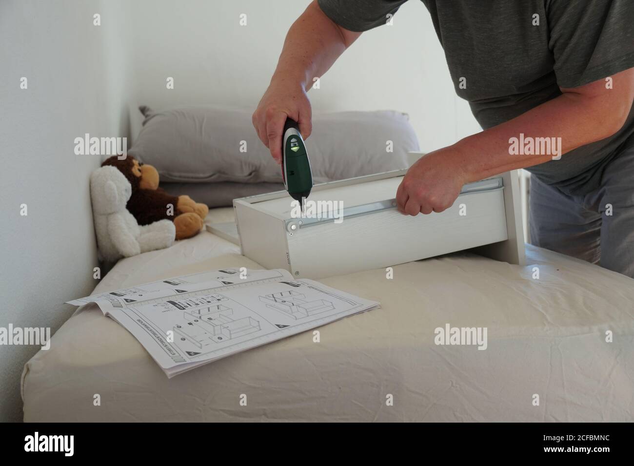 Ein Mann, der mit einem Akkuschrauber eine Schublade eines Computerschreibtisches für seinen Sohn zusammengebaut hat. Er verwendet ein Werkzeug und Anweisungen, um das Projekt abzuschließen. Stockfoto