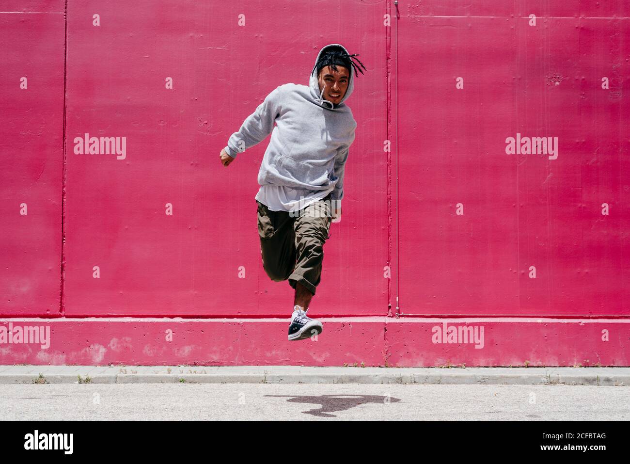 Junge hispanische Männer springen nahe an eine rosa Wand Die Straße Stockfoto