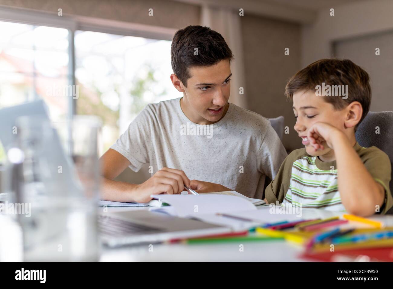Teenager Junge hilft seinem jüngeren Bruder Hausaufgaben zu Hause Stockfoto