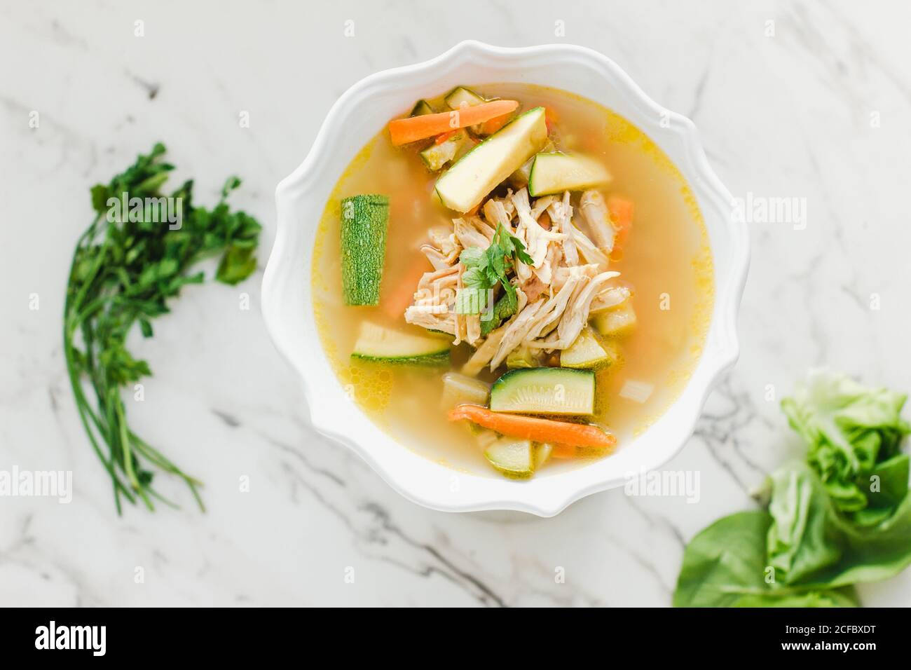 Serviert Schüssel mit Hühnersuppe mit Karotten, Koriander und Zucchini auf dem Tisch Stockfoto