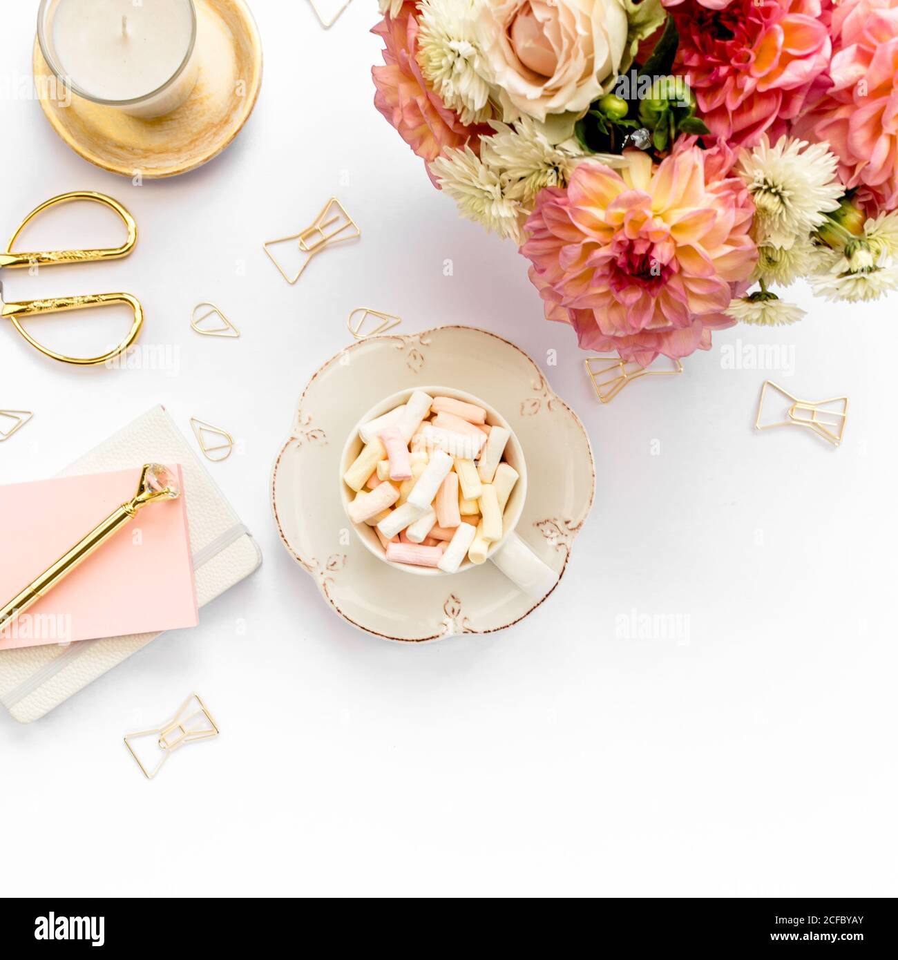 Flacher Büroschreibtisch. Weiblicher Arbeitsplatz mit rosa Rosen, Dahlien Blumen Bouquet, goldene Accessoires, Tagebuch auf weißem Hintergrund. Draufsicht. Stockfoto