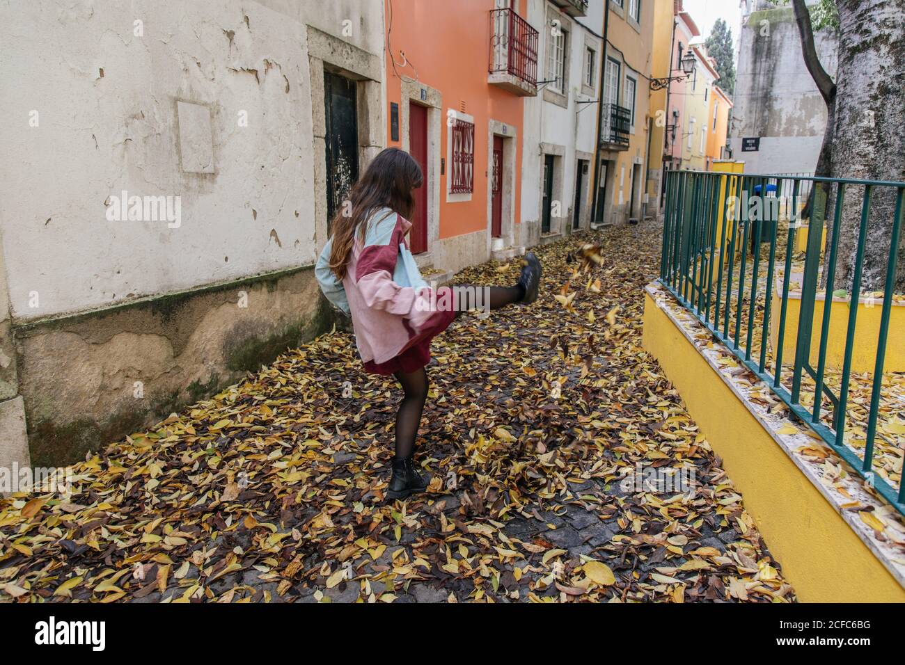 Rückansicht anonyme, aktive junge Frau, die beim Spaziergang in der Straße von Lissabon Herbstblätter tritt Stockfoto