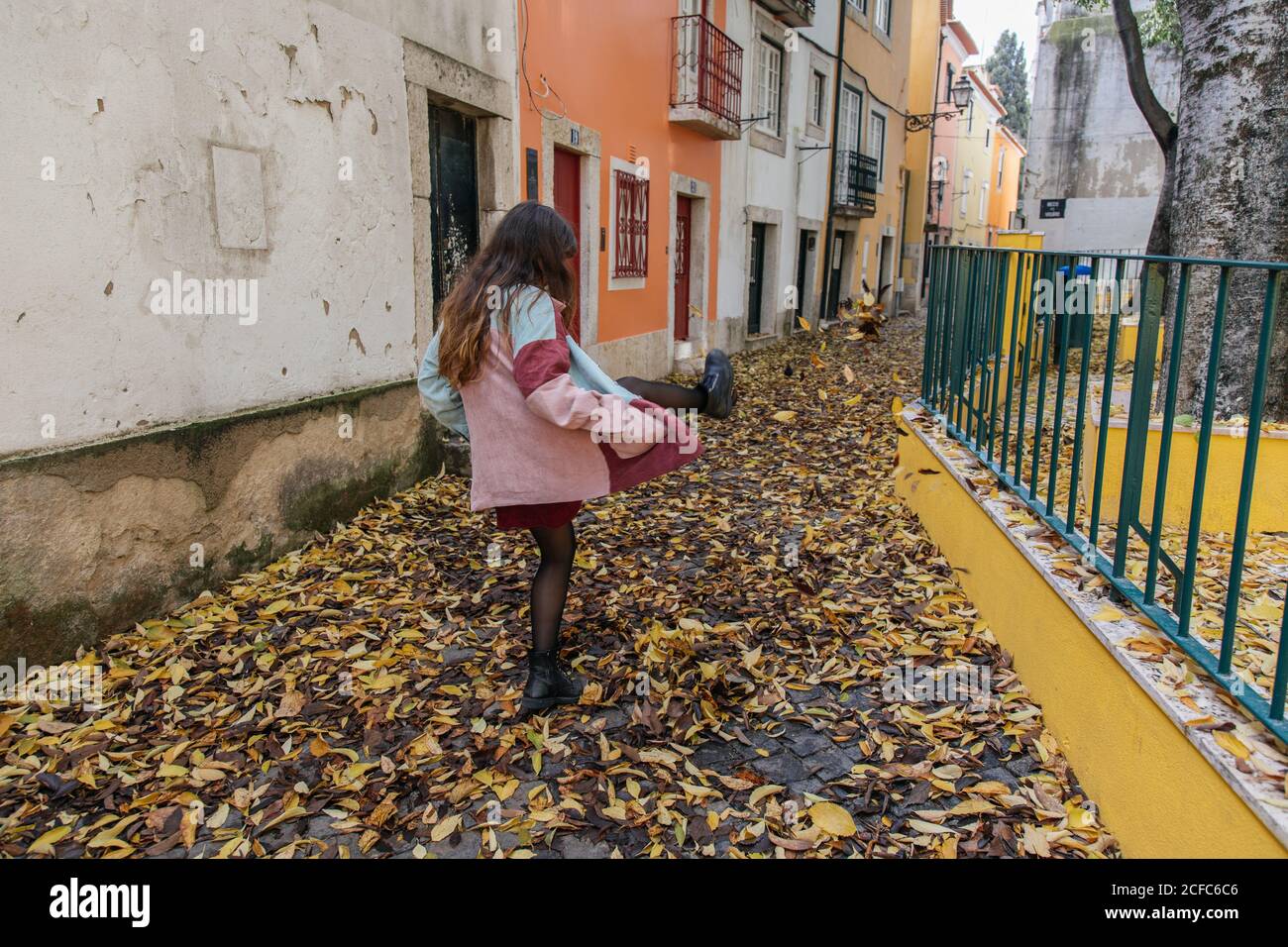 Rückansicht anonyme, aktive junge Frau, die beim Spaziergang in der Straße von Lissabon Herbstblätter tritt Stockfoto