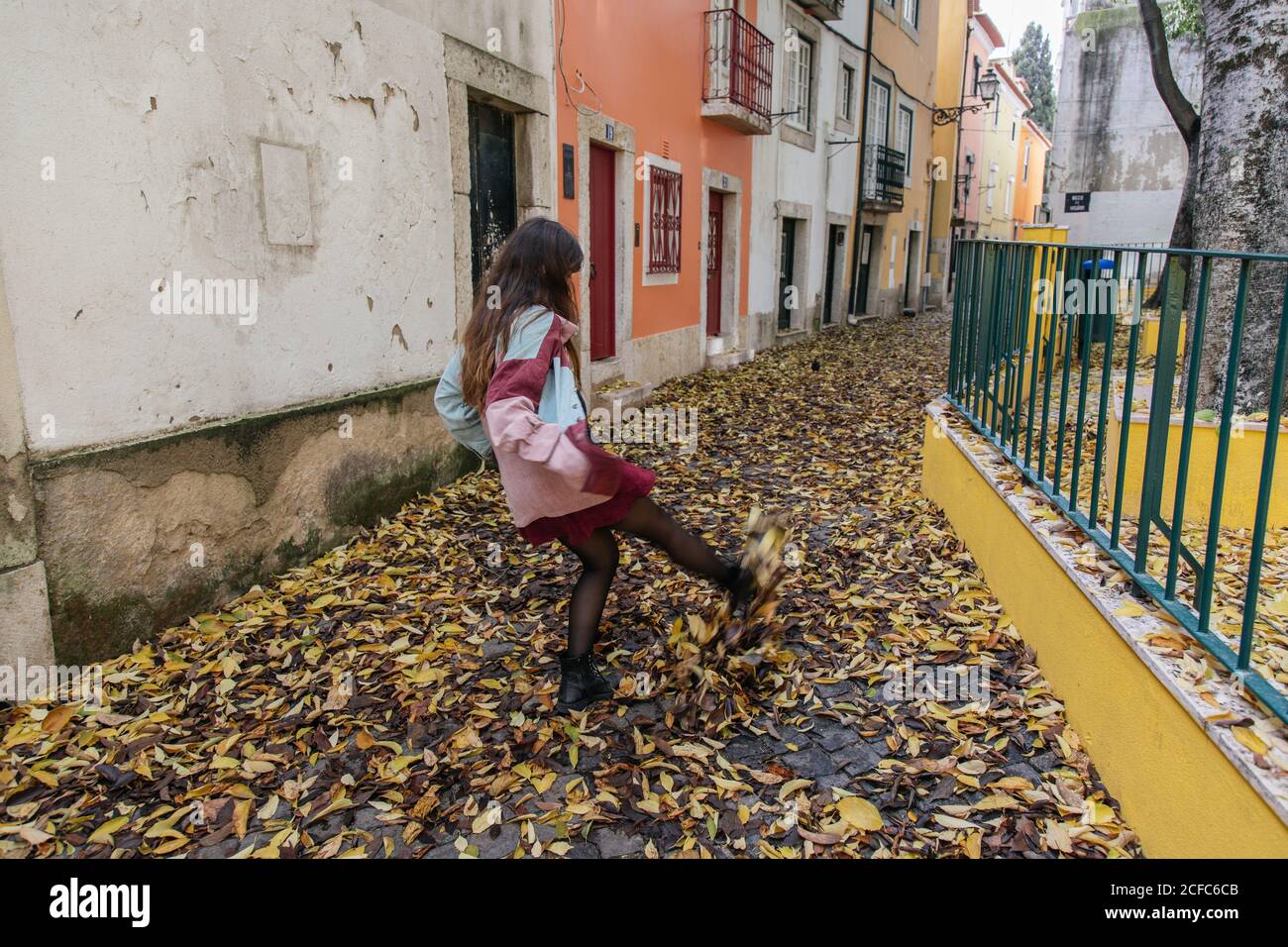 Rückansicht anonyme, aktive junge Frau, die beim Spaziergang in der Straße von Lissabon Herbstblätter tritt Stockfoto
