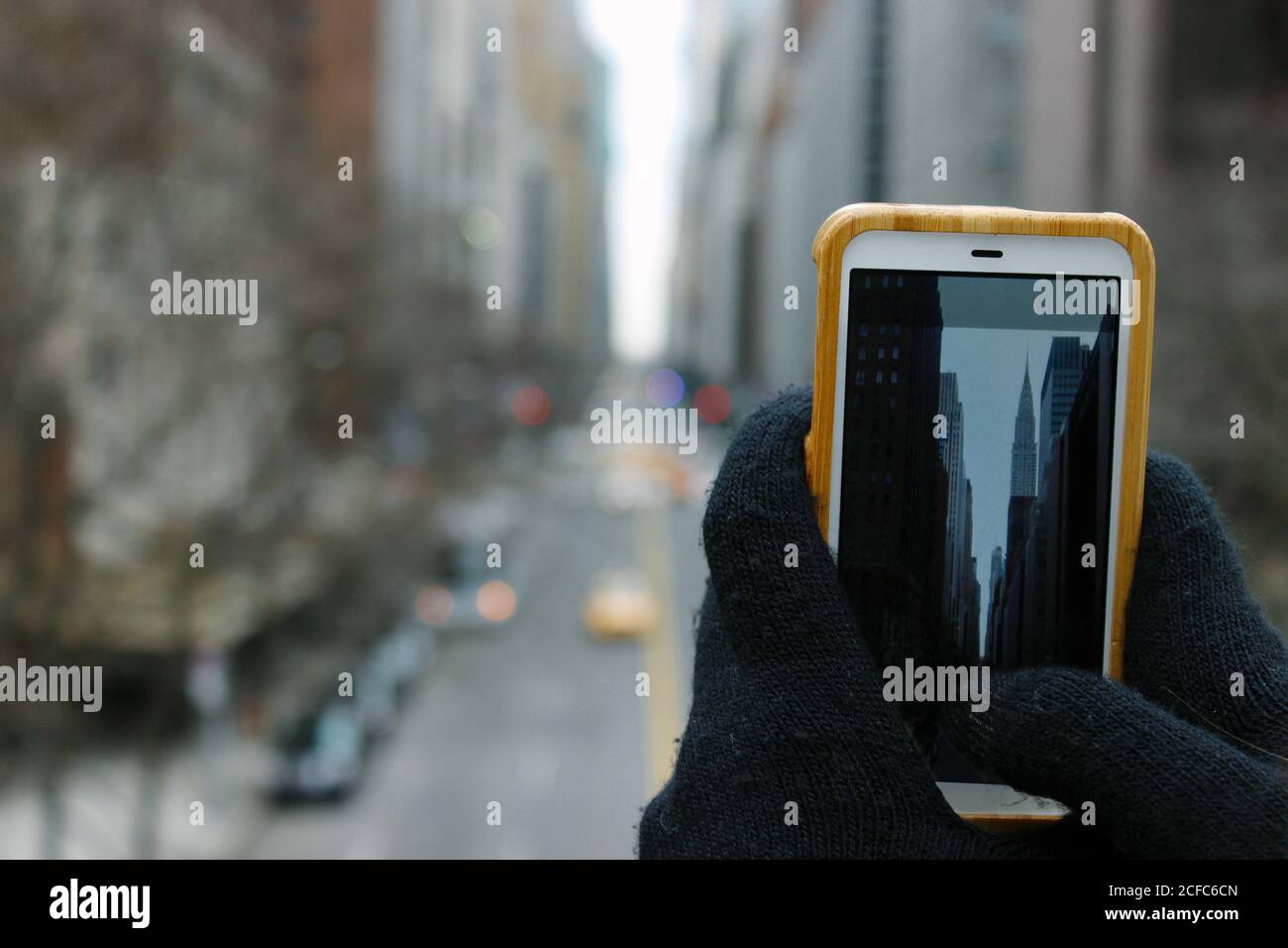Tourist hält Smartphone mit beiden Händen, während die Stadtbild von Wolkenkratzer in New York im Winter Stockfoto