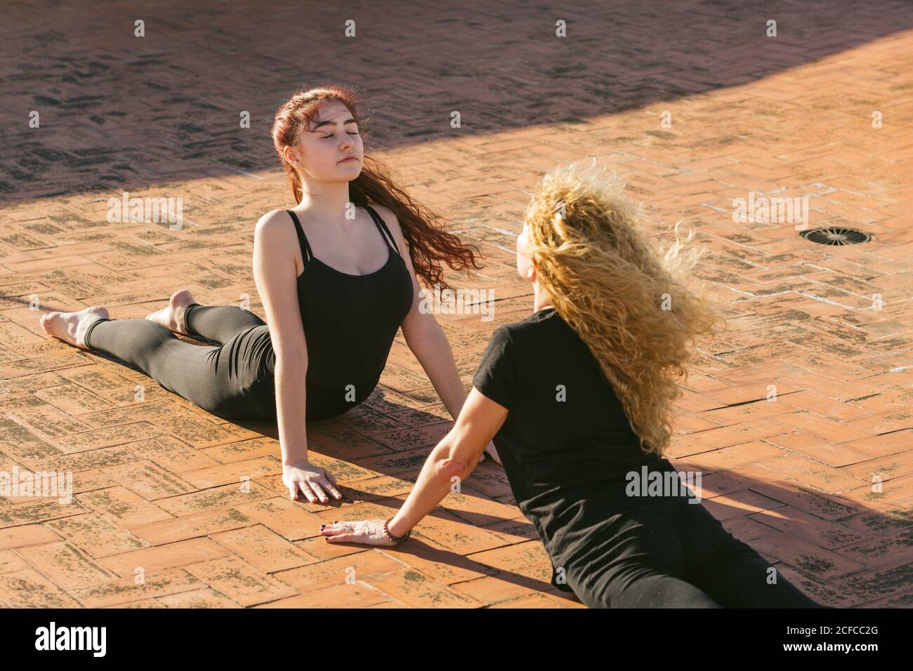 Hoher Winkel von jungen und mittleren Alters Frauen in schwarz Sportbekleidung, die Cobra posiert, während sie gemeinsam Yoga bei Sonnenschein praktiziert Terrasse Stockfoto