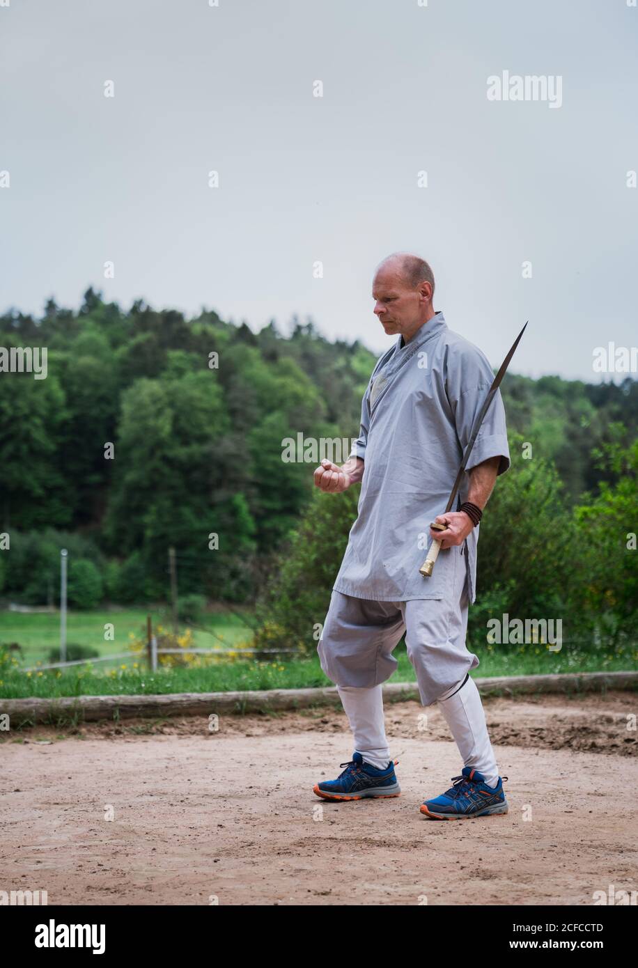 Bestimmt Mann mittleren Alters in Kimono Fokussierung und mit Schwert Beim Training allein im Garten Stockfoto