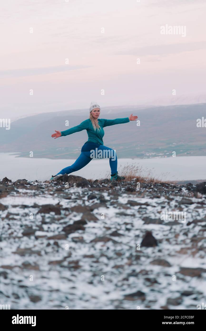 Seitenansicht einer blonden Frau mit hochgepupptem Bein und von Hand zu Seite posiert sie auf dem Berg im Schnee Stockfoto