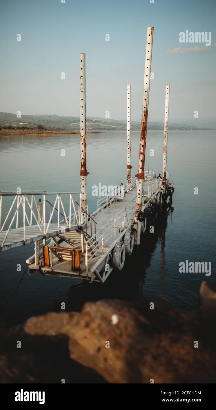 Alte rostige Pier mit entfernten Touristen in der Nähe des friedlichen Meeres Wasser in der Dämmerung Stockfoto