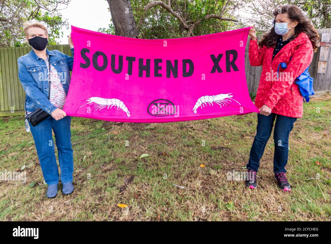 Extinction Rebellion Southend Zweigstelle, XR, protestiert am Flughafen gegen Flugreisen. Zwei maskierte Frauen halten Banner mit Garnelen-Symbole Stockfoto